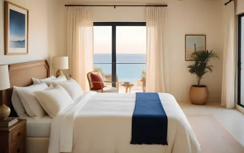 Acogedores dormitorios estilo mediterráneo con vistas al mar. Cama blanca con manta azul, sillón de mimbre y plantas.
