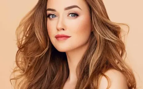 Mujer con cabello castaño dorado, ondulado y con reflejos claros. Su mirada es penetrante y sus labios pintados de rosa.