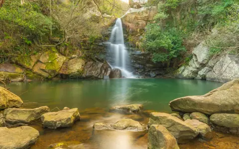 Cascada en un entorno verde con aguas cristalinas, evocando la belleza de las piscinas naturales de Cádiz.