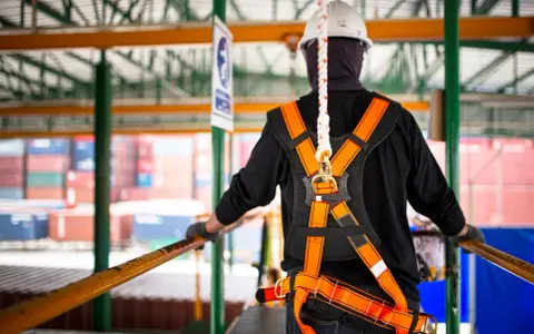 Trabajador con arnés de seguridad naranja y blanco, listo para trabajar en altura. La vida útil de un arnés de seguridad depende de su uso y mantenimiento.