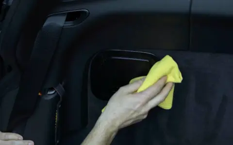Hand wischt mit gelbem Tuch über schwarzes Kunstleder im Auto. So einfach ist Kunstleder reinigen.
