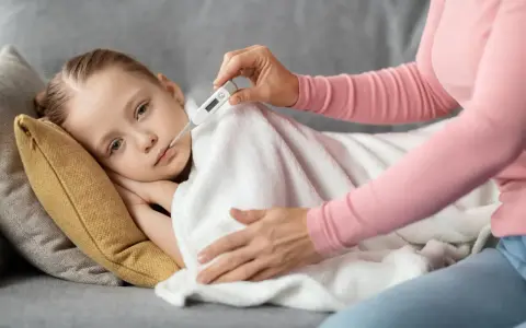 Dziecko leży pod kocem, mama mierzy mu temperaturę. Wysoka gorączka u dziecka bez innych objawów martwi.
