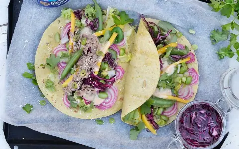 Två läckra tonfisk wraps fyllda med grönsaker, rödlök och en krämig sås. En burk med rödkålssallad står bredvid.