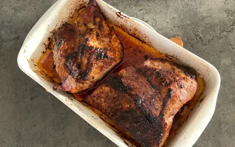 Två saftiga bitar av grillad pluma ligger i en vit ugnsform, redo att serveras.