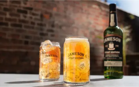 Dwa orzeźwiające drinki z lodem i butelka Jameson Stout Edition na tle ceglanej ściany.