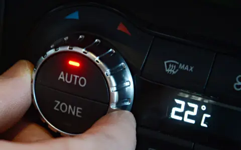 Hand dreht am Regler der **Klimaanlage Auto** auf 22 Grad Celsius. Rote LED leuchtet.