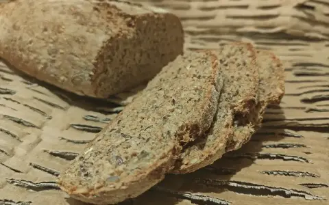 Chleb orkiszowy, pokrojony w kromki, z widocznymi ziarnami, leży na falistej tekturze.