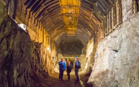 Trzech turystów w kaskach oświetla latarkami mroczny tunel kopalni. Czy to osówka czy włodarz, kto tu mieszka?