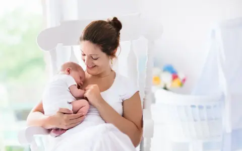 Uśmiechnięta mama kołysze śpiące dziecko. Gratulacje z okazji narodzin dziecka!