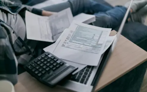 Osoba przegląda dokumenty podatkowe, kalkulator i laptop. Analiza składnik zmienny stawki sieciowej.