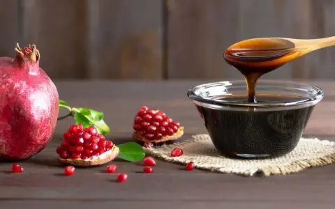 Granaty i gęsty, ciemny sos z granatów w miseczce i na drewnianej łyżce.