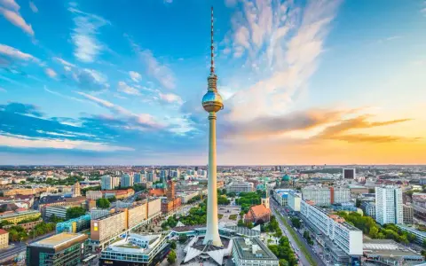 Der Berliner Fernsehturm mit seiner Aussichtsplattform ragt über die Stadt. Ein dramatischer Himmel mit Wolken und Abendsonne umrahmt das Wahrzeichen.