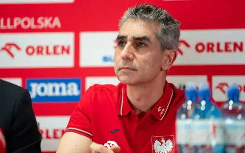 Trener reprezentacji Polski w piłce ręcznej, w czerwonej koszulce z orłem, podczas konferencji prasowej.
