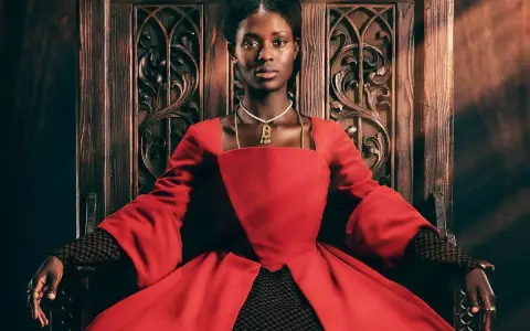 Jodie Turner-Smith, con su mirada regia, se sienta en un trono de madera tallada, vestida con un opulento traje rojo.