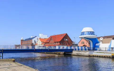 Port rybacki nad Wieprzą z niebieskim mostem i charakterystycznym budynkiem w kształcie statku kosmicznego.