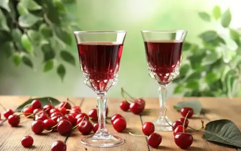 Dwa kieliszki z rubinową, szybką nalewką z wiśni na spirytusie, otoczone świeżymi wiśniami na drewnianym stole.