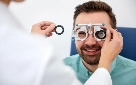 Mężczyzna uśmiecha się podczas badania wzroku w domu. Optometrysta wymienia soczewki w oprawce próbnej.