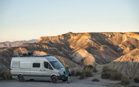 Ein Campervan steht in der Wüste Spaniens, bereit für wildcampen. Die Sonne beleuchtet die zerklüfteten Berge im Hintergrund.