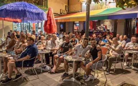 People enjoying drinks at outdoor tables outside gay bars in Sitges, Spain.