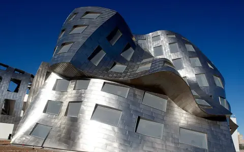 Edificio dalle forme ondulate e metalliche, una delle opere di Frank Gehry, con finestre quadrate e rettangolari.