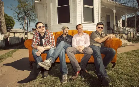 Cuatro hombres sentados en un sofá naranja, como si fueran **track dogs** esperando su próxima aventura.