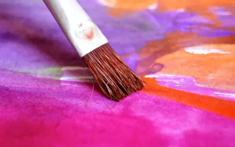 Pinceau humide sur une toile aux couleurs vives, mélangeant le pastel sec et l'eau pour créer des dégradés vibrants de rose, violet et orange.