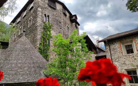 Il castello di Campo Tures, con le sue mura in pietra e il tetto a scandole, si erge maestoso tra il verde e fiori rossi.