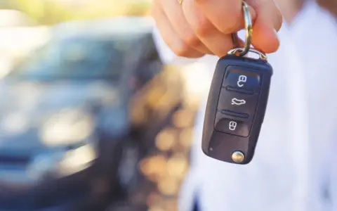 Dłoń trzyma kluczyk samochodowy z ikonami otwierania, bagażnika i zamykania. Kontrolka immobilizera na kluczyku jest gotowa do uruchomienia pojazdu.