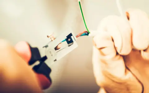 Manos con guantes pelando cables para como cambiar el termostato de la calefacción.