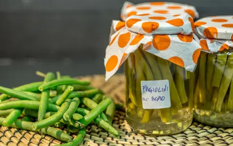 Fagiolini sott'olio in agrodolce, conservati in barattoli con tappi decorati. Freschi e pronti per essere gustati.