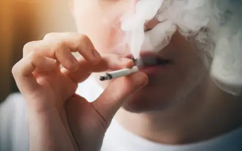 Persona fumando un cigarrillo, exhalando humo denso. Podría ser un indicio de sobredosis de nicotina.