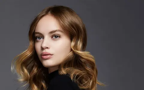 Porträt einer jungen Frau mit welligem, braunem Haar, das mit Balayage-Technik aufgehellt wurde.