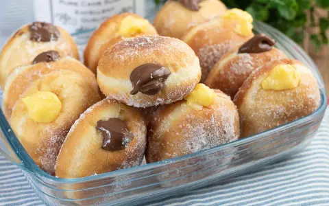 Bomboloni ricetta originale ripieni di crema e cioccolato, cosparsi di zucchero. Un dolce invitante pronto da gustare.