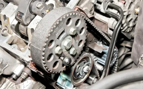Zbliżenie na mechanizm rozrządu silnika, widoczny jest czujnik położenia wałka rozrządu, koło pasowe i pasek.