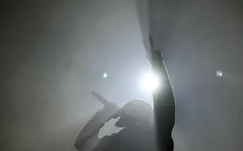 Un rappeur, micro en main, lève un doigt en signe de paix. Lumière intense, fumée, ambiance d'un exposé sur le rap.