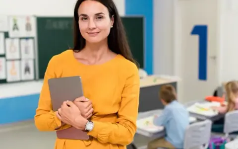 Nauczycielka z tabletem w klasie, przygotowująca się do zajęć. Jej pasja do pracy z dziećmi zaowocowała studiami podyplomowymi nauczyciel wspomagający.