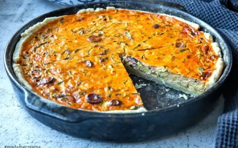 Herzhaftes Quiche Rezept mit Zucchini und Oliven, goldbraun gebacken in einer Gusseisenpfanne. Ein Stück ist bereits herausgeschnitten.