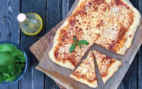 Pyszna pizza margherita z ciągnącym się serem i świeżą bazylią, obok butelka oliwy i miseczka ziół.