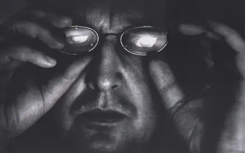 Portret Krzysztofa Gierałtowskiego w okularach, z dłońmi przy twarzy.