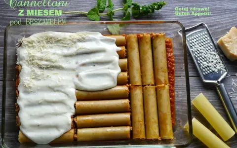 Cannelloni z mięsem mielonym i sosem beszamelowym w naczyniu żaroodpornym, gotowe do pieczenia. Obok tarka i kawałek parmezanu.