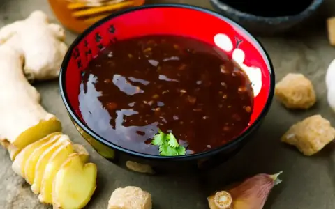 Sos teriyaki przepis: miseczka pełna aromatycznego sosu, obok świeży imbir, czosnek i brązowy cukier. Idealny do dań azjatyckich.