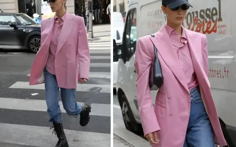 Kobieta w marynarce w odcieniu **magenta kolor** i jeansach idzie ulicą. Czapka z daszkiem i okulary dodają jej miejskiego stylu.