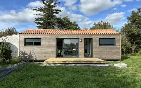 Une petite maison en bois avec une terrasse, idéale pour un plan maison 5m sur 10m. Le toit est couvert de tuiles rouges.