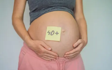 Brzuch kobiety w ciąży z karteczką "40+". To dowód, że ciąża po 40. jest możliwa i piękna.