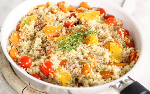 Salade de quinoa colorée avec carottes, tomates cerises et quartiers d'orange, garnie de thym. Un plat savoureux qui met en avant les quinoa bienfaits.