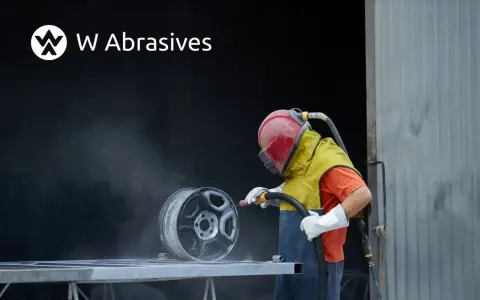 Pracownik w kasku i ochronnym ubraniu wykonuje piaskowanie aluminium felgi.