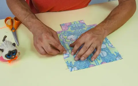 Mains assemblant deux pièces de tissu fleuri, parfait pour une idée couture débutant. Ciseaux et un chat porte-épingles à proximité.