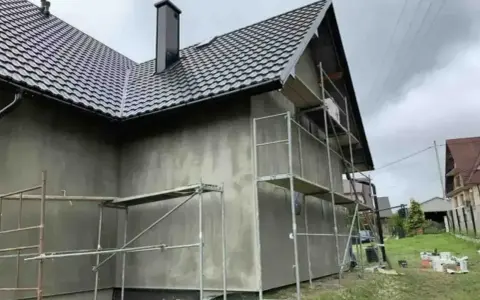 Dom w trakcie prac elewacyjnych. Widać rusztowania i szarą ścianę, która czeka na tynk silikonowy. Cena za m2 robocizny jest kluczowa dla budżetu.