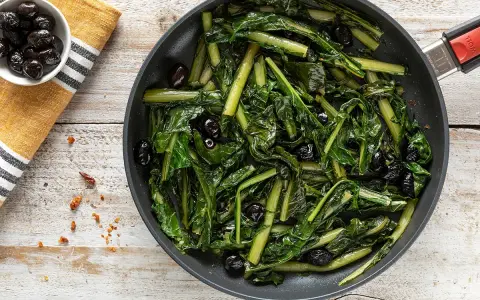 Verdura di catalogna saltata in padella con olive nere. Un piatto semplice e gustoso, pronto per essere servito.