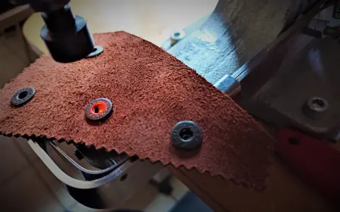 Narzędzie do mocowania zatrzasków do kurtki na brązowym materiale. Pokazuje, jak założyć zatrzaski do kurtki, przygotowując materiał.